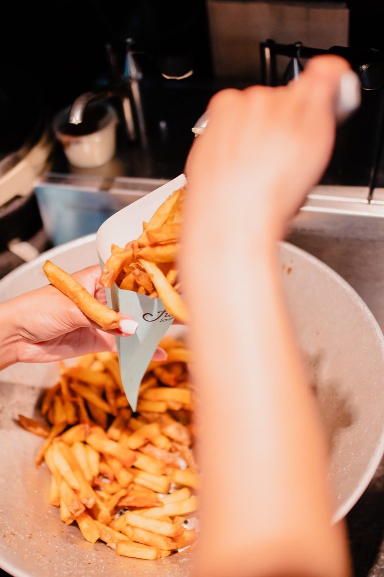 Handen pakken verse friet uit een bak